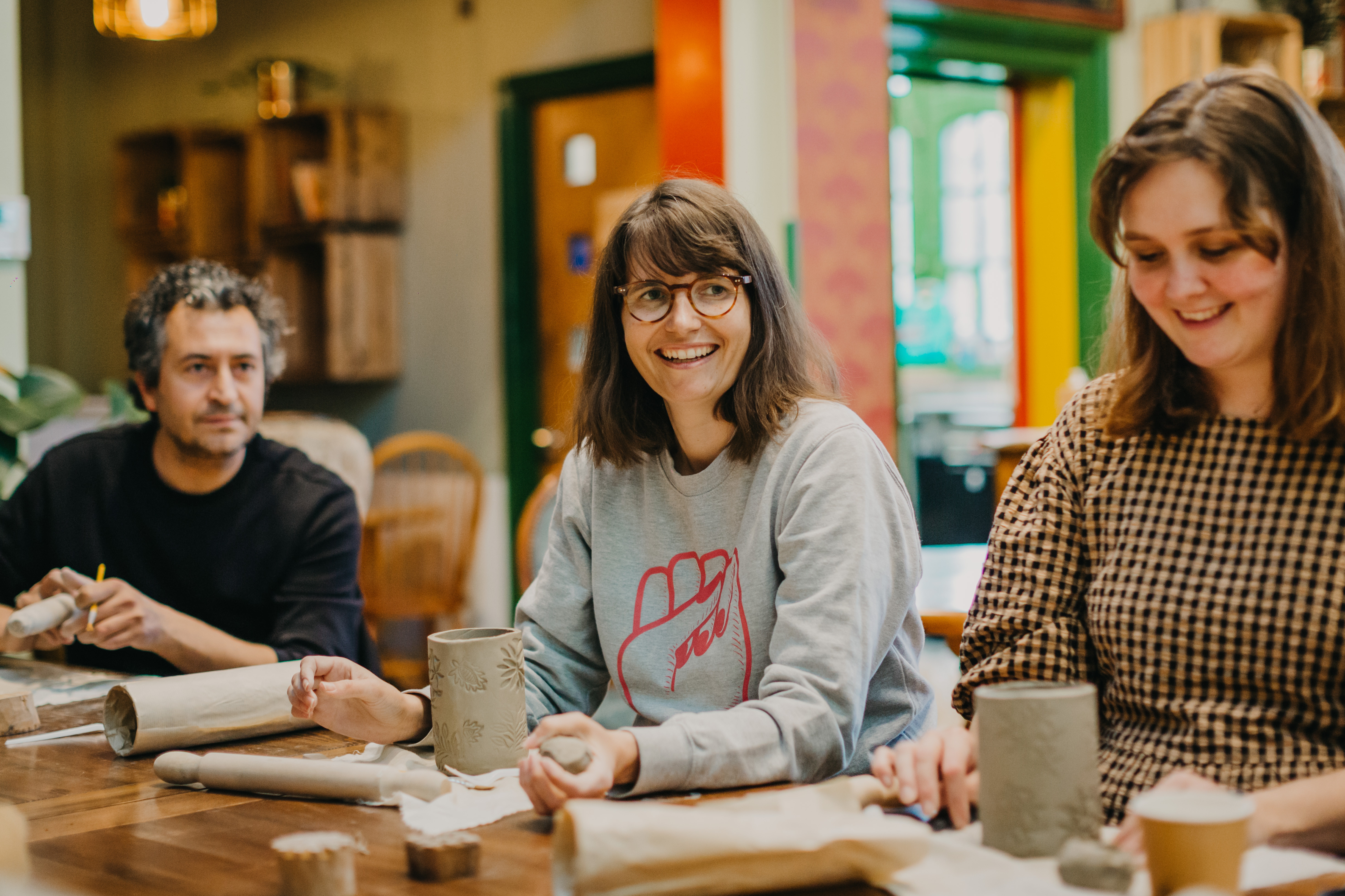 Three people smiling and laughing at a pottery class